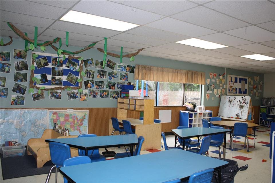 Empty classroom with blue tables and chairs, maps, and photos on the walls