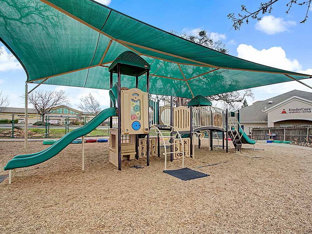 Playground with climbing structure, slides, and green shade cover