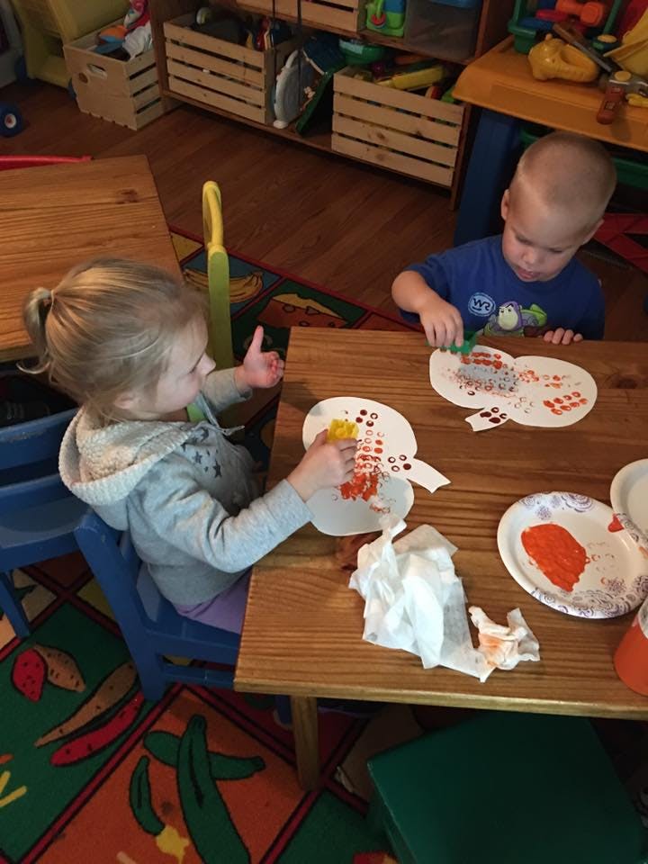 Two children sitting at a table doing crafts with crafts with paper cutouts and paint