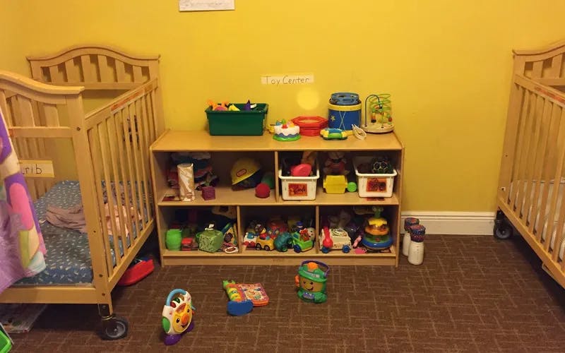 Two cribs and a shelf unit filled with toys in a room
