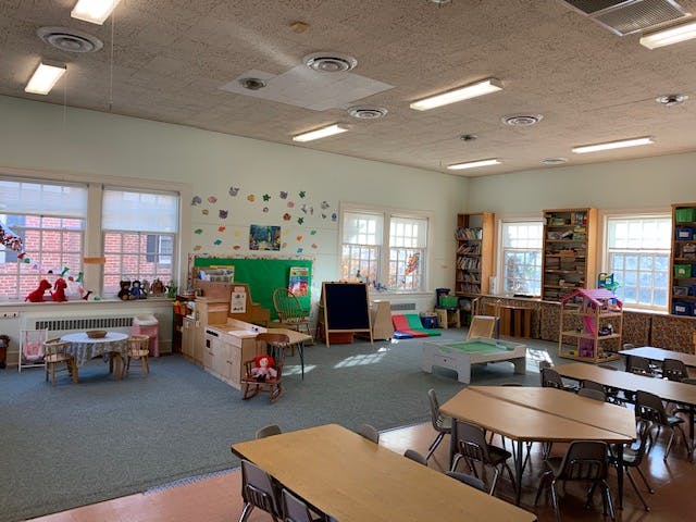 Classroom with small tables and chairs, bookshelves, and a chalkboard
