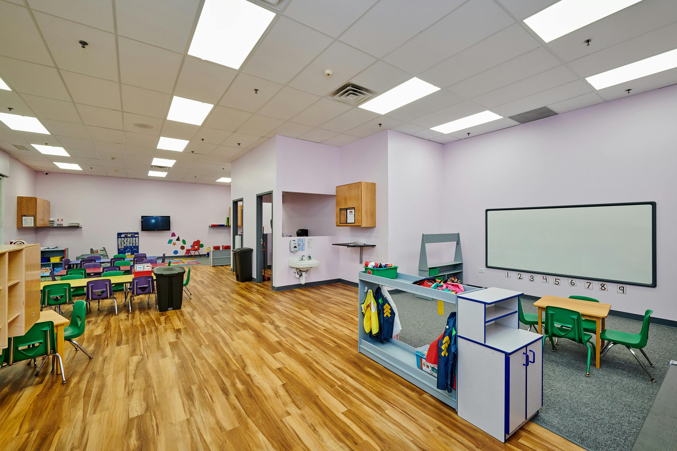 Empty classroom with small tables and chairs, a whiteboard, and storage units