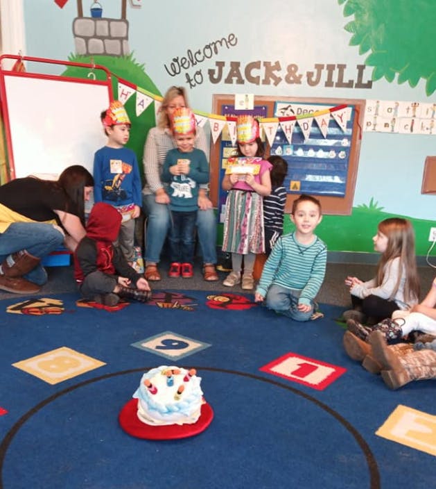 Adults and children in a classroom with a cake on a cake on the floor