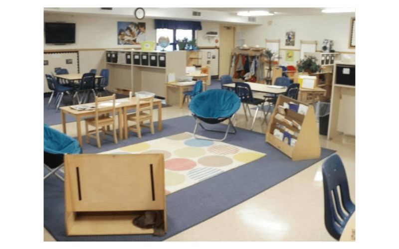 Classroom with small tables, chairs, a circular rug, and a blue beanbag chair