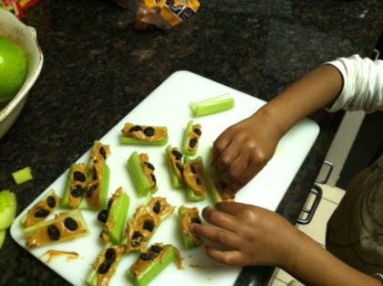 Child's hands arranging celery sticks with peanut butter and raisins