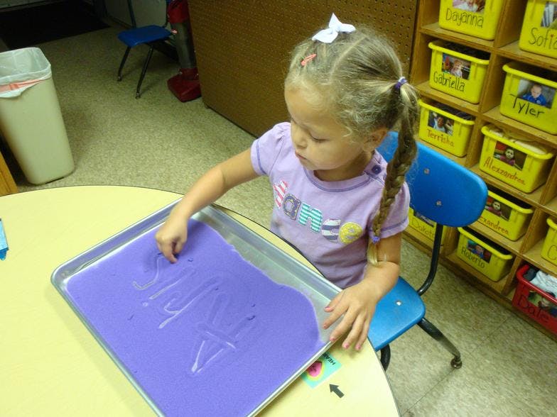 Child drawing in purple sand on a tray