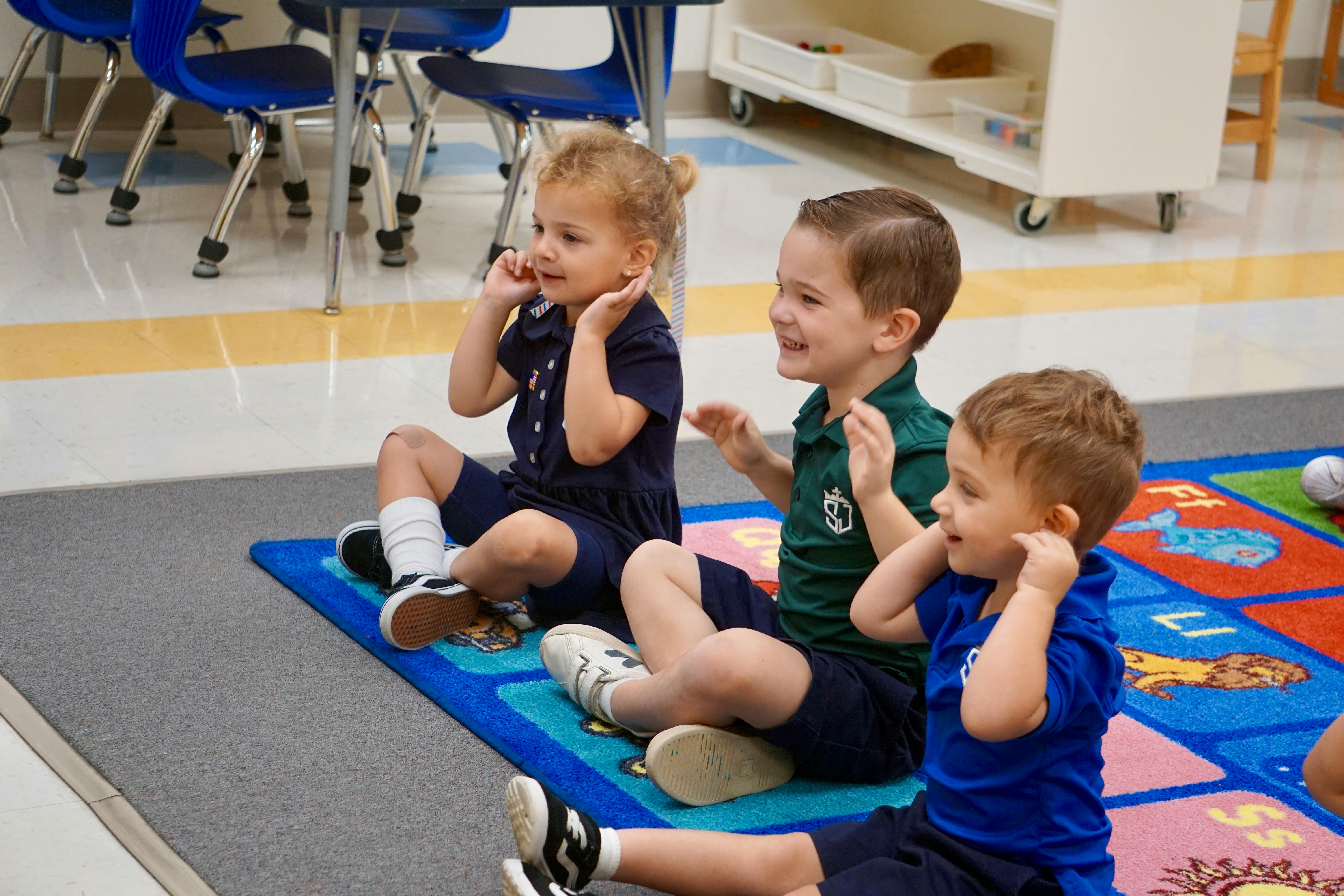 Three children sitting on a rug in a classroom