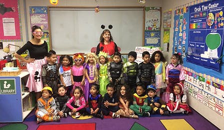 Two adults and multiple children in costumes in a classroom