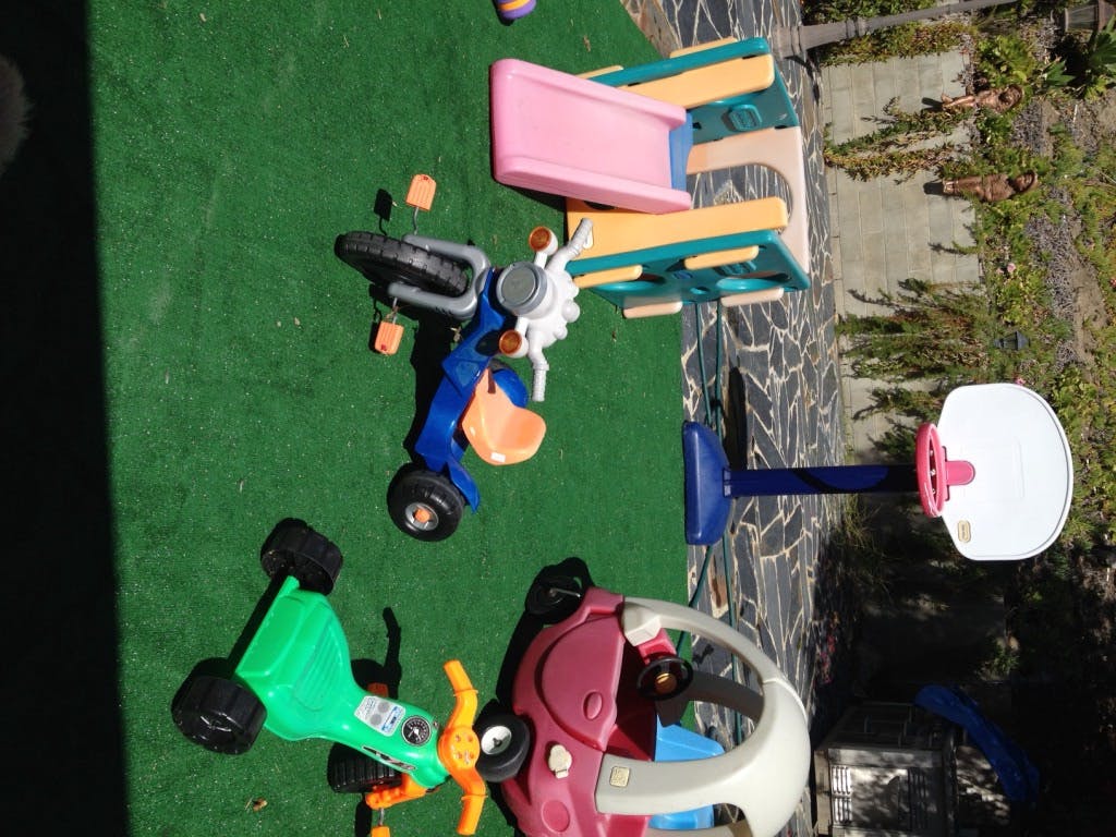 Children's toys including a scooter, tricycle, and basketball hoop on artificial grass