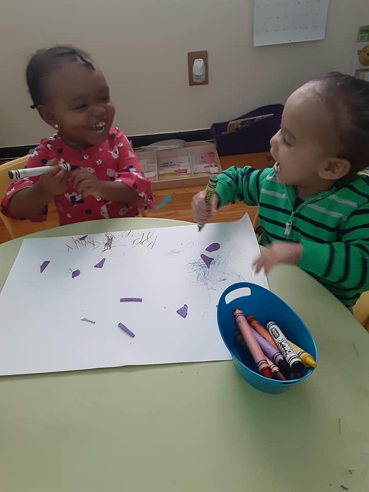 Two children drawing on paper with crayons