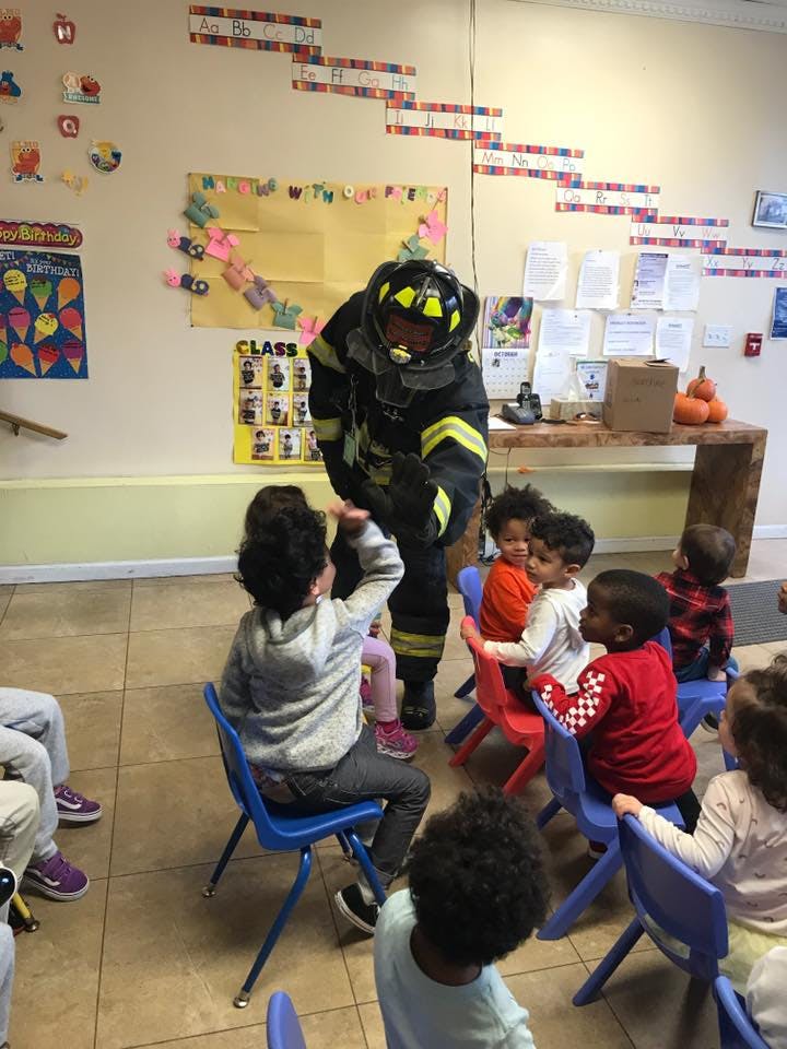 Person in firefighter gear interacting with children in a classroom