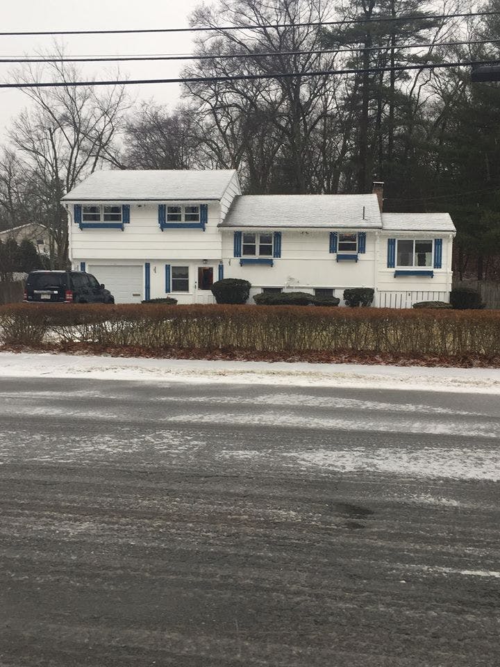 White house with blue shutters and a black vehicle in the driveway