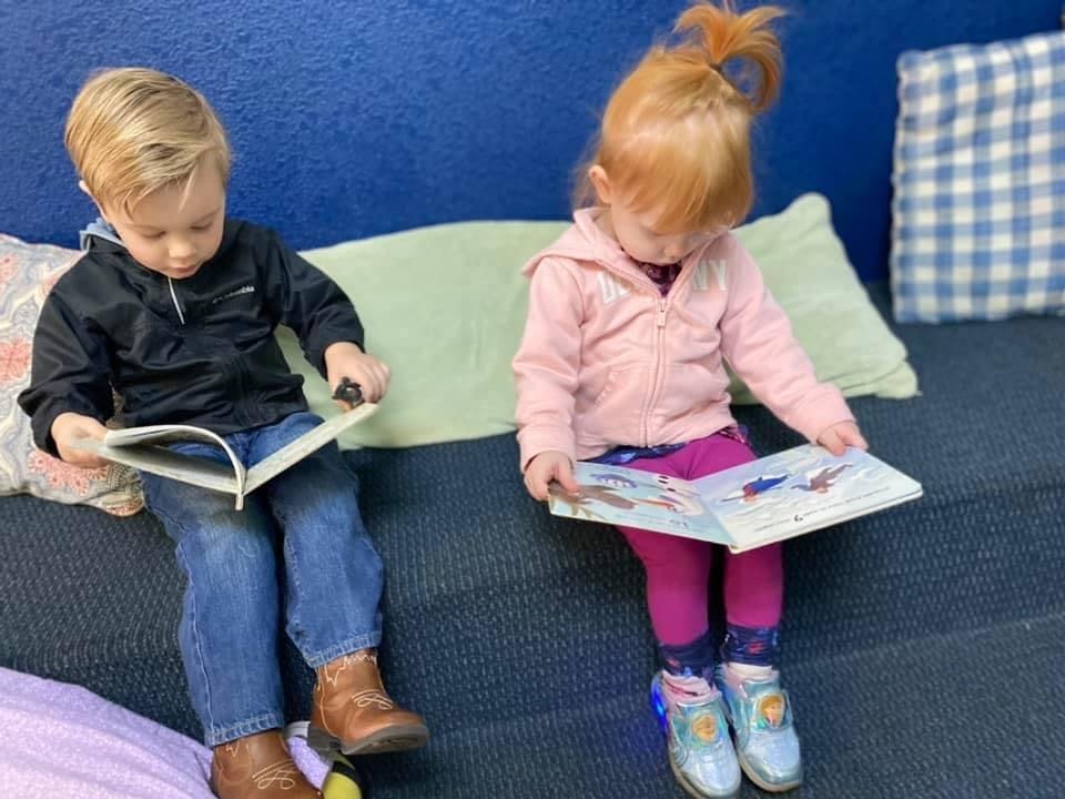 Two children sitting on a couch reading books