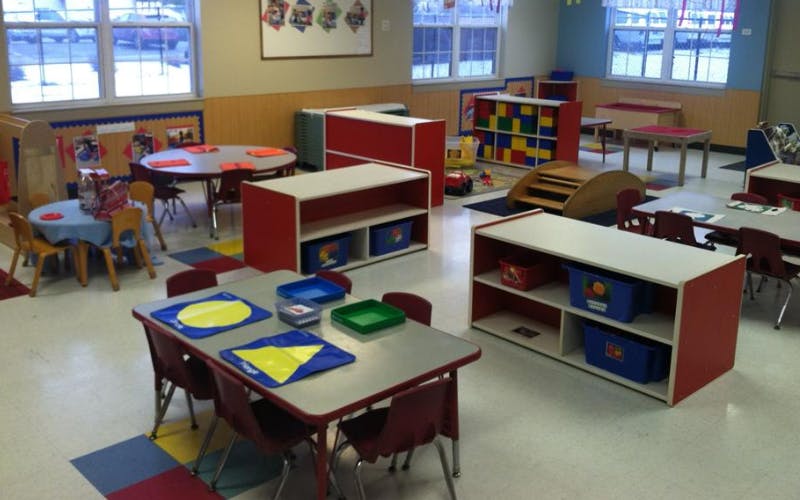 Classroom with child-sized tables and chairs, shelves with bins, and windows