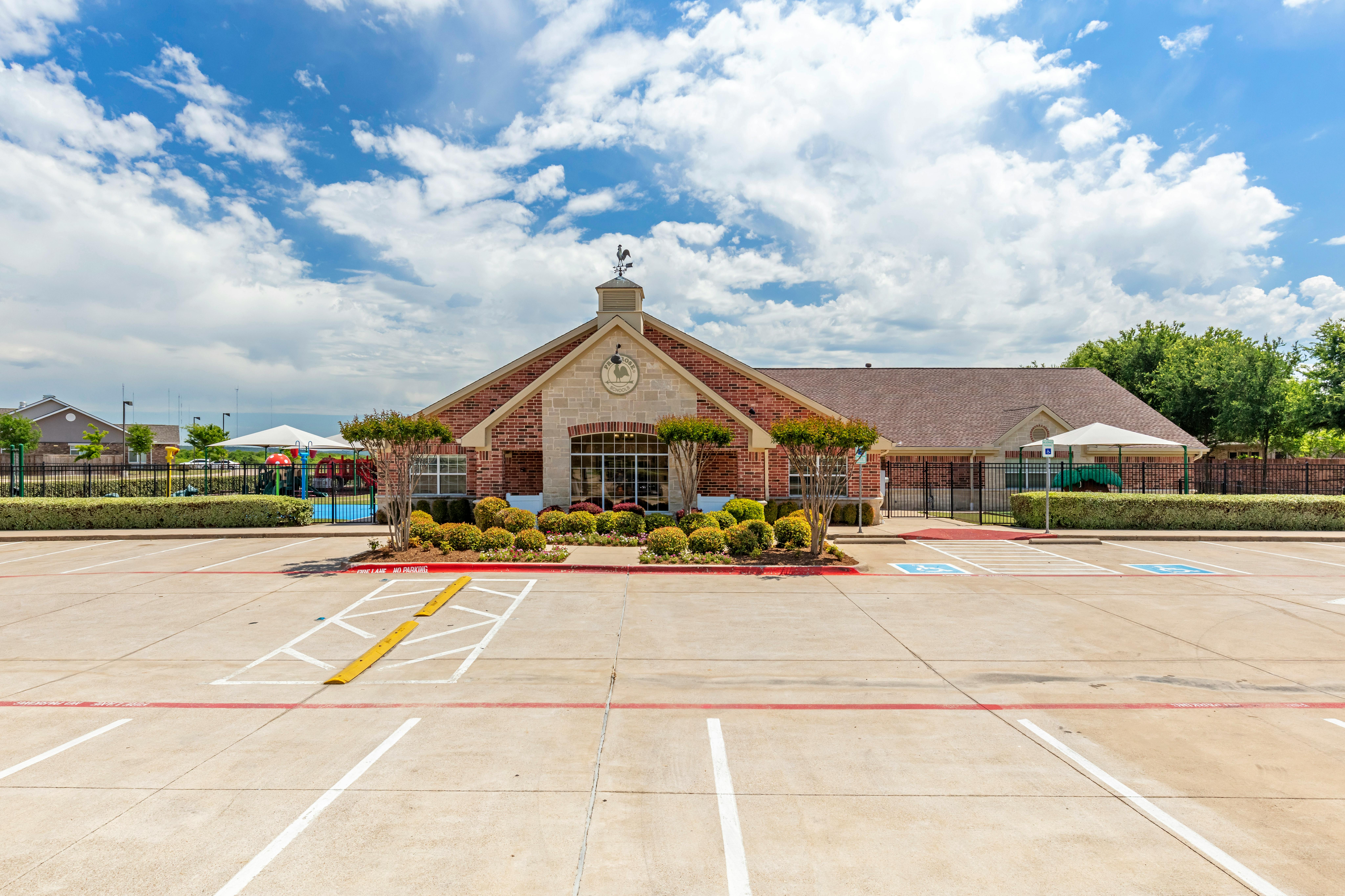 Brick building with a weather vane on the roof and a playground behind a fence