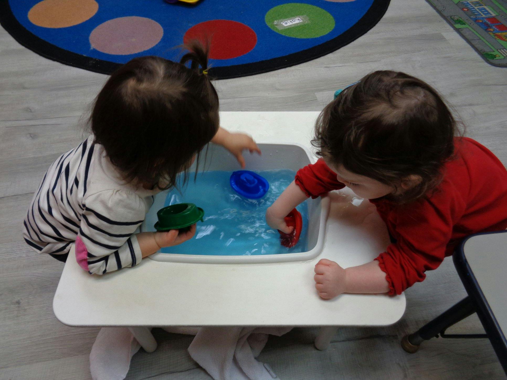 Two children playing with toy boats in a water table