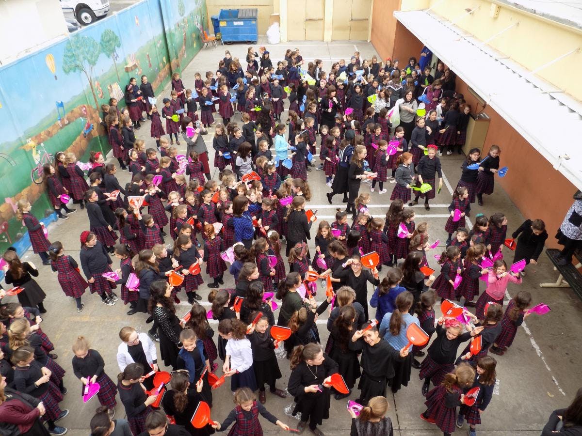 Large group of children holding dustpans in an outdoor area