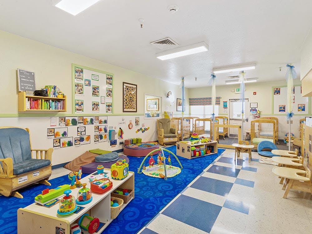 An empty infant classroom with cribs, play mats, and toys