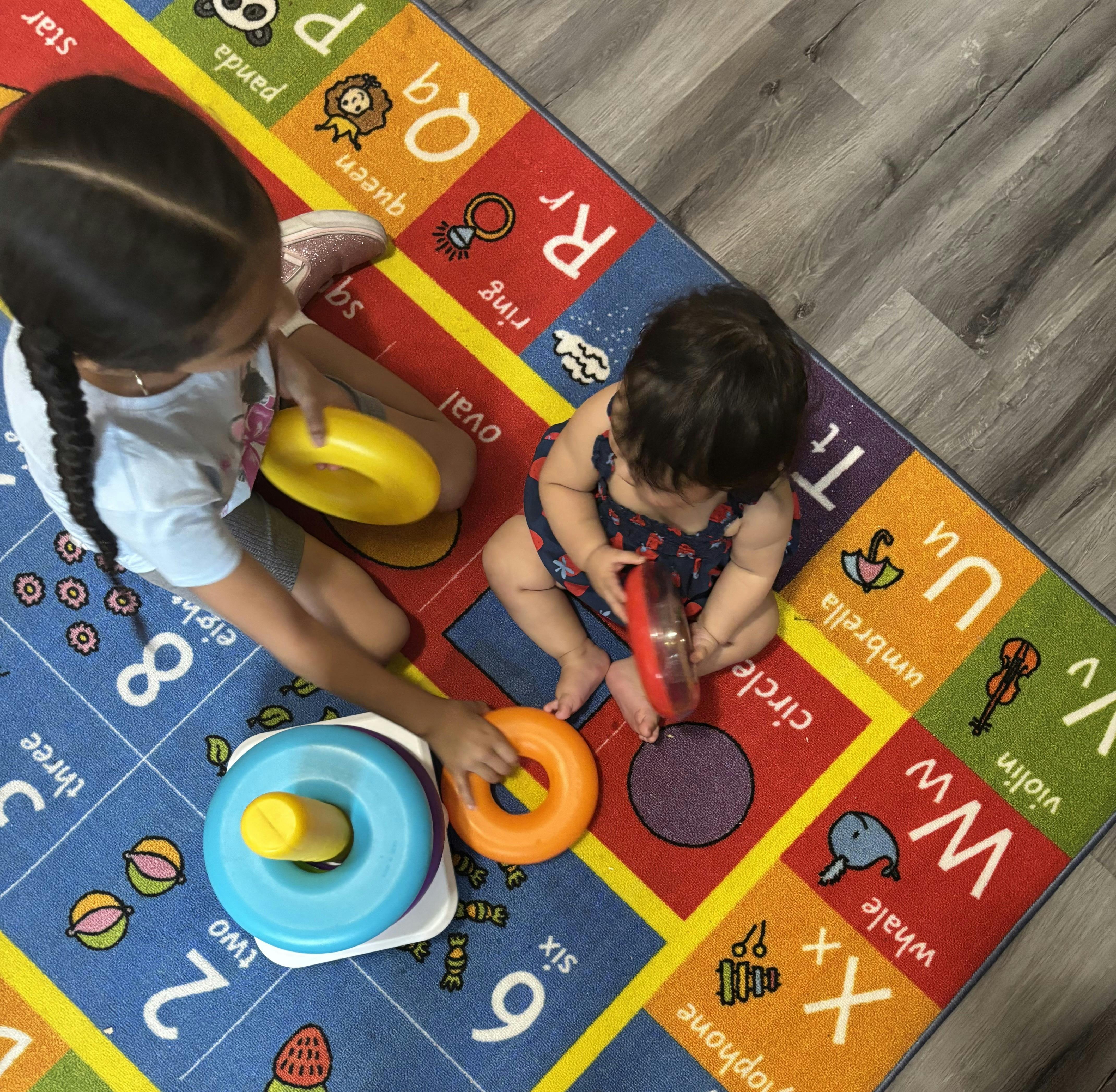 Child and baby playing with stacking rings on an alphabet mat