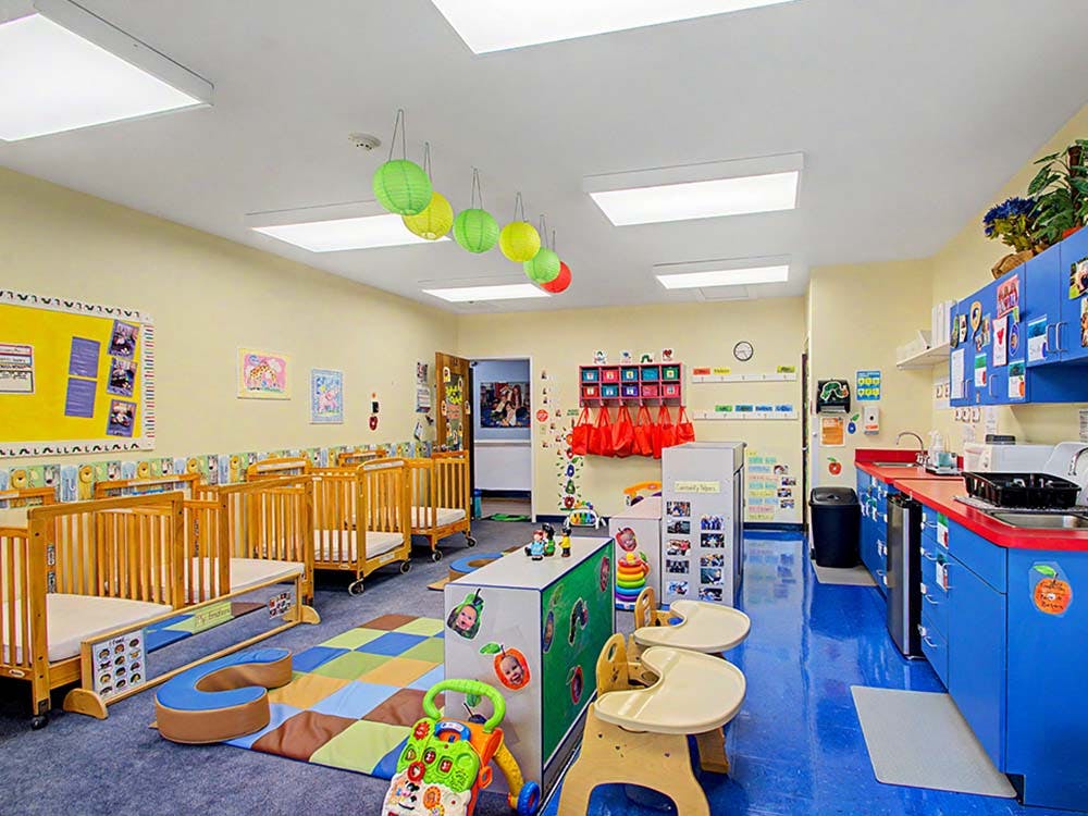 daycare classroom with multiple cribs, a play mat, and a counter with sinks
