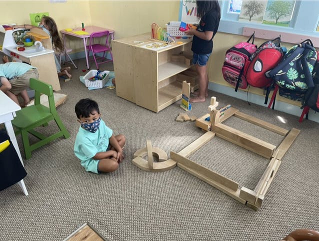 Child wearing a mask sitting on the floor next to wooden blocks
