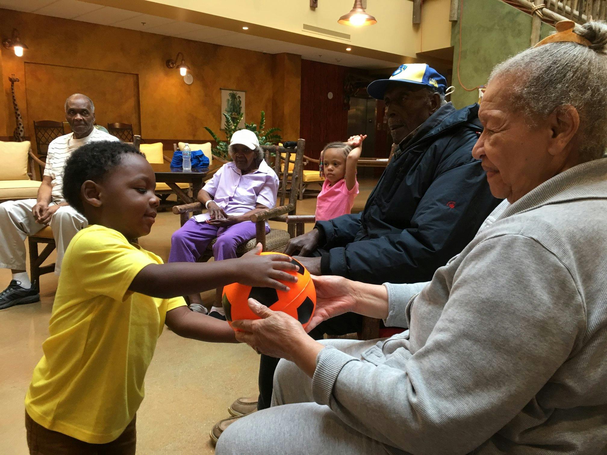 Child in yellow shirt handing an orange ball to an adult