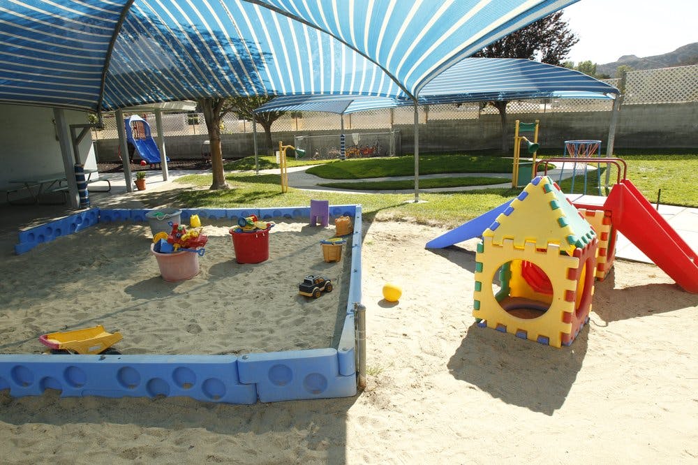 Sandbox with toys and a playhouse with a slide under a striped canopy