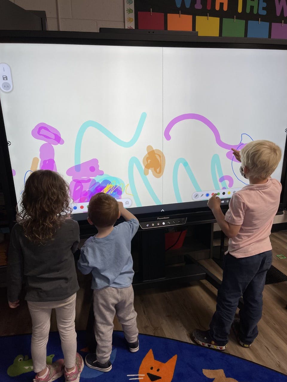 Three children drawing on a large interactive screen