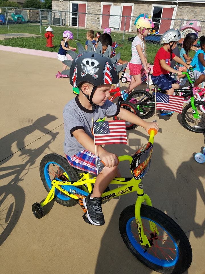 Child on a bicycle with an American flag, wearing a helmet