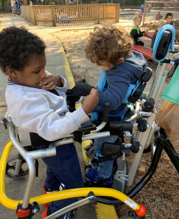 Two children in adaptive equipment interacting outdoors