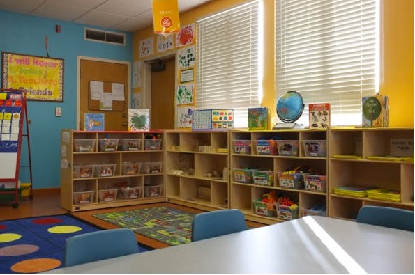 Classroom with shelves of toys and books, colorful rugs, and a table with chairs