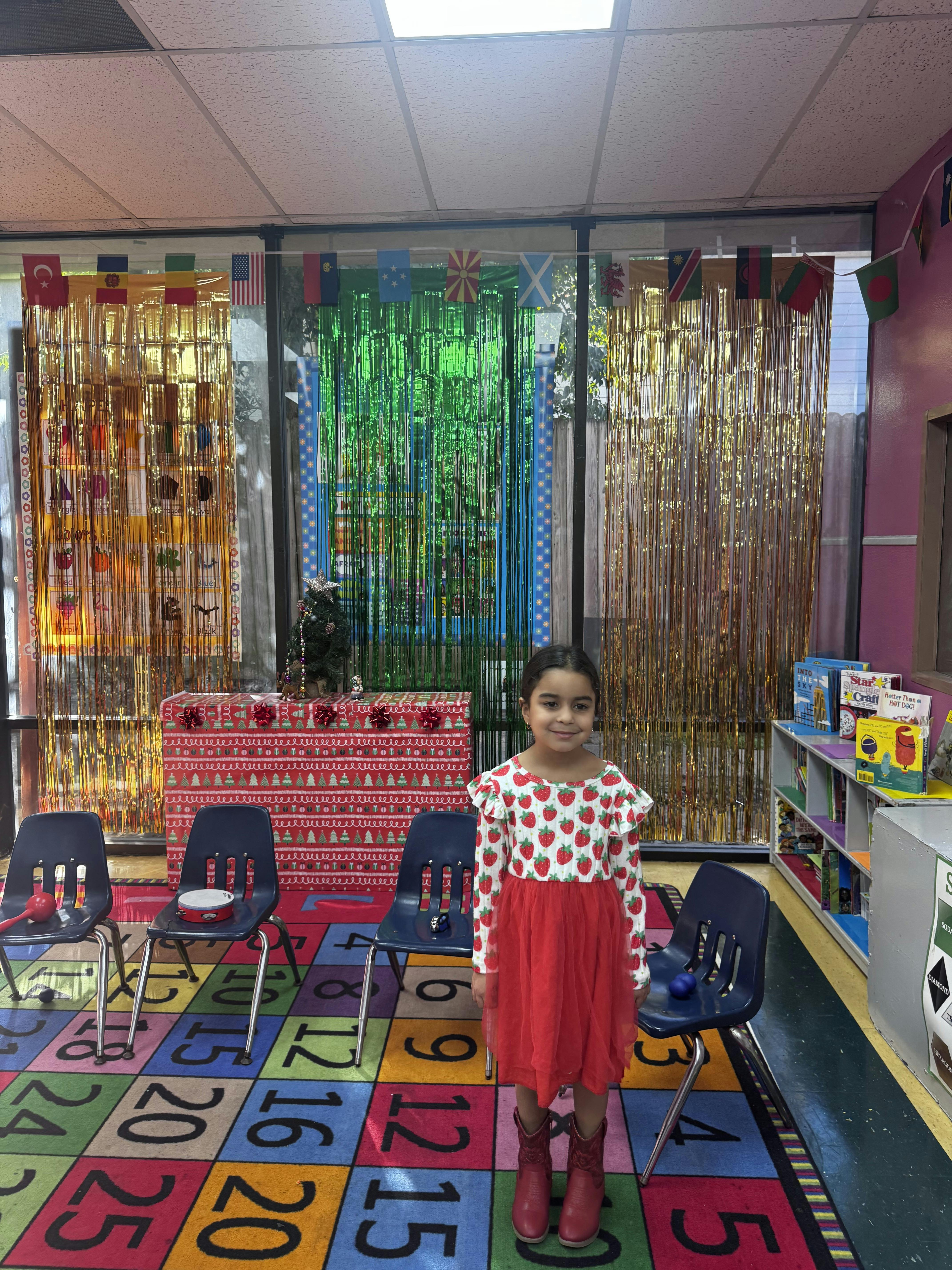 Child in a red dress with strawberry print top standing in a classroom
