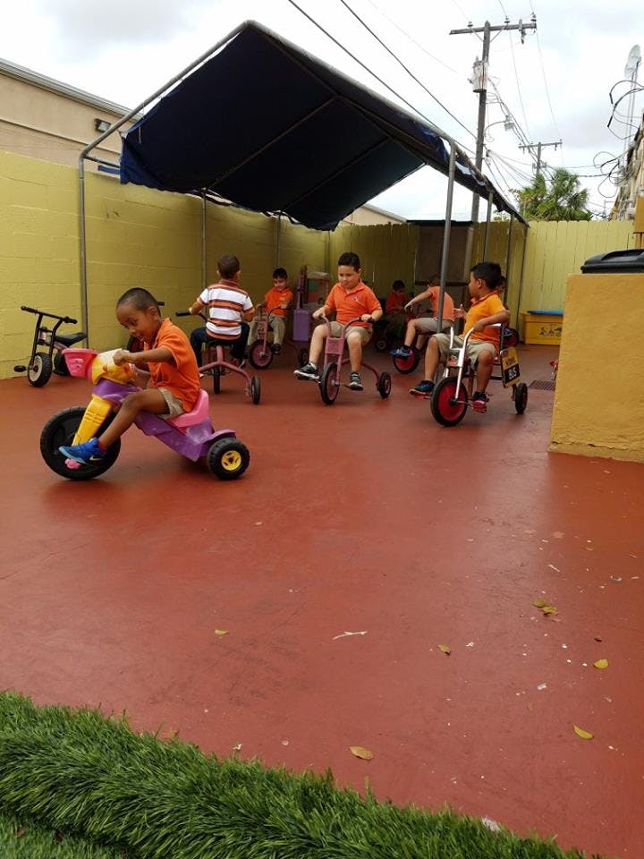 Children riding tricycles on a red surface under a canopy