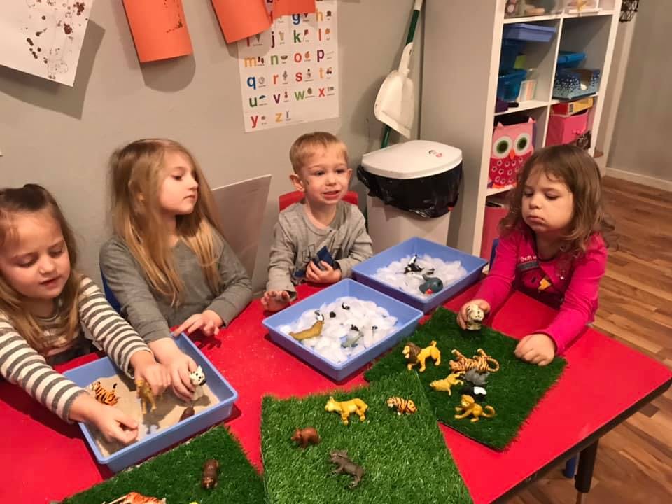 Four children playing with animal figurines and sensory bins at a table