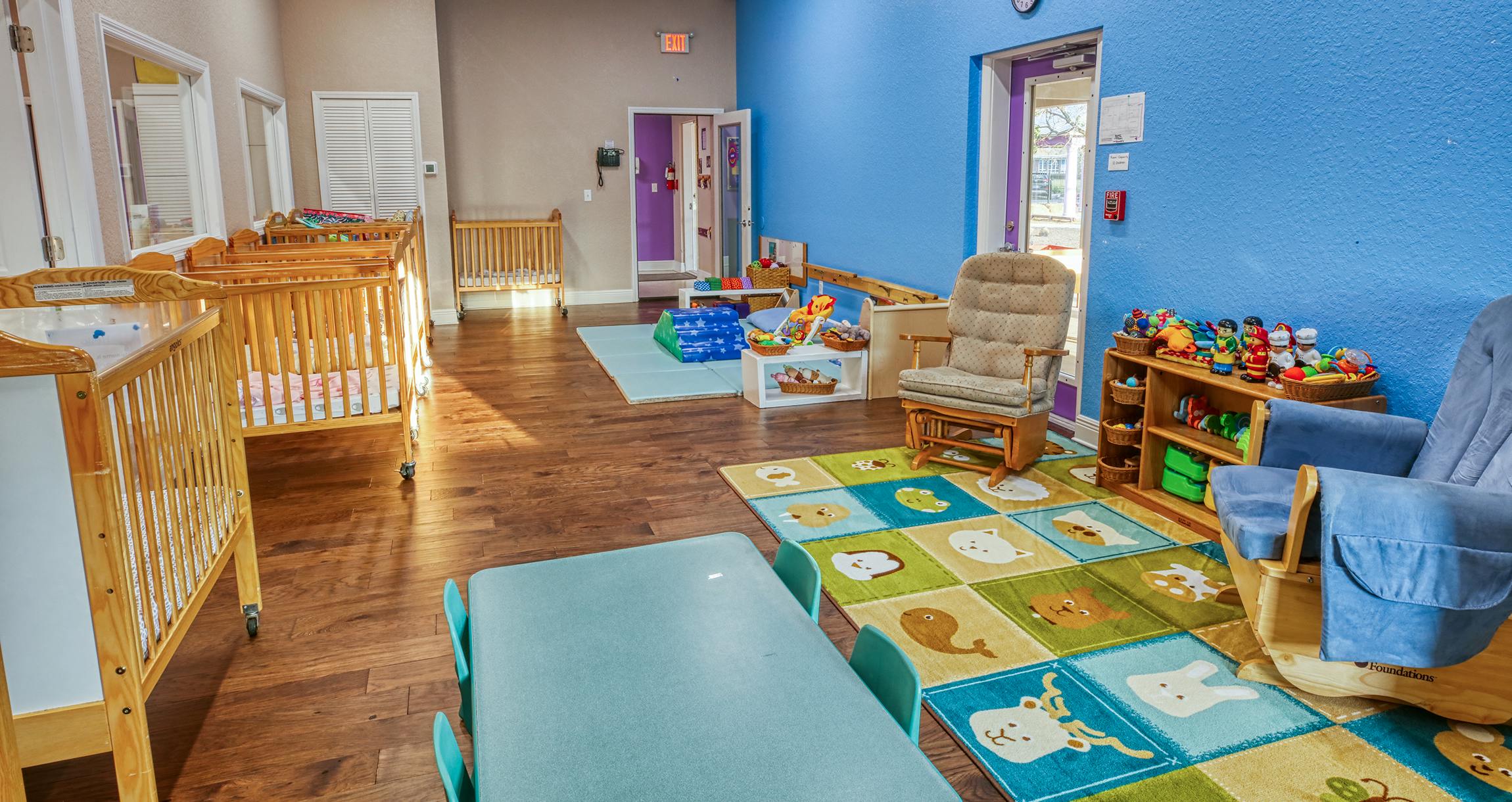 Cribs, play mats, and a small table in a daycare room