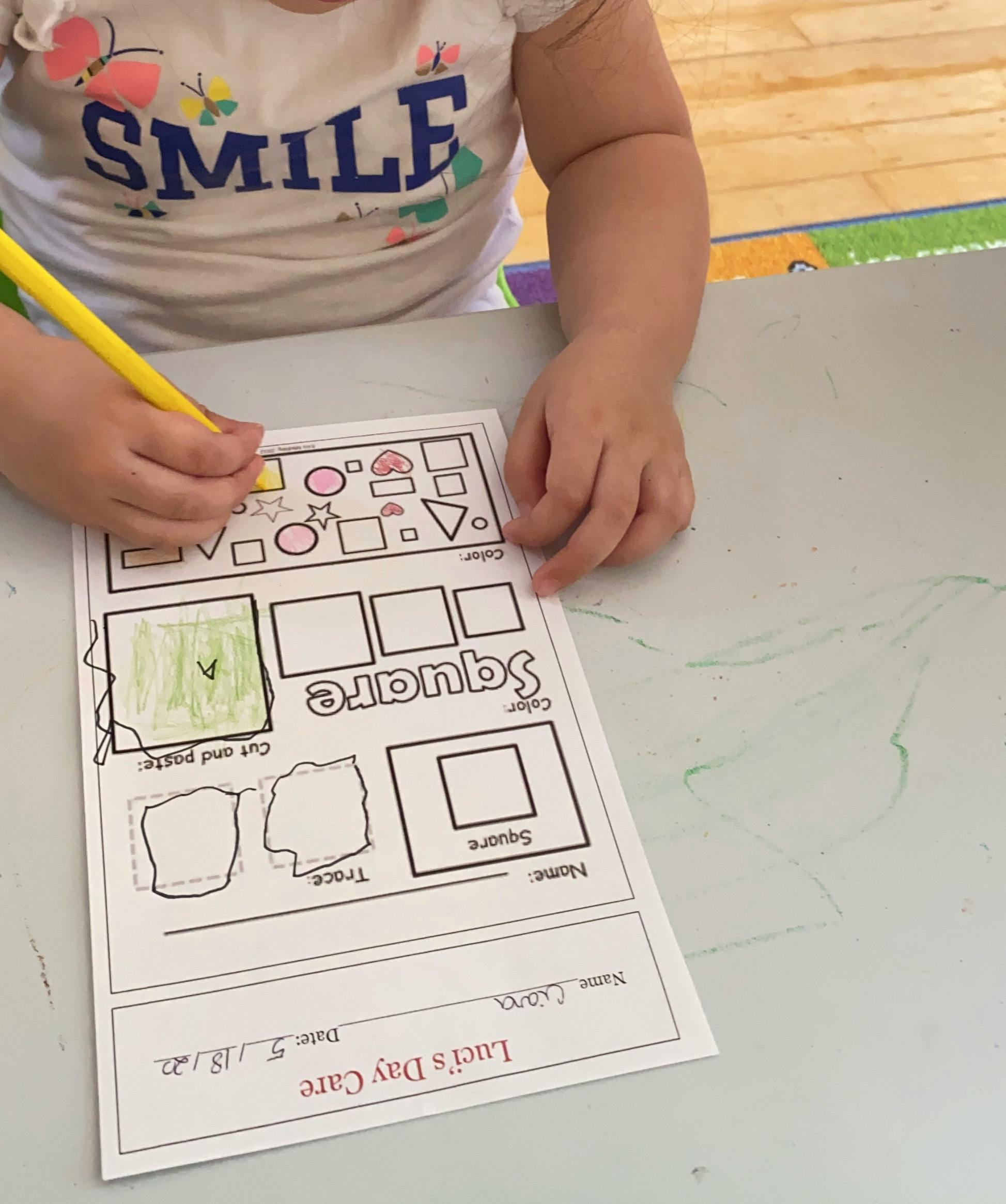 Child coloring a worksheet with a yellow crayon