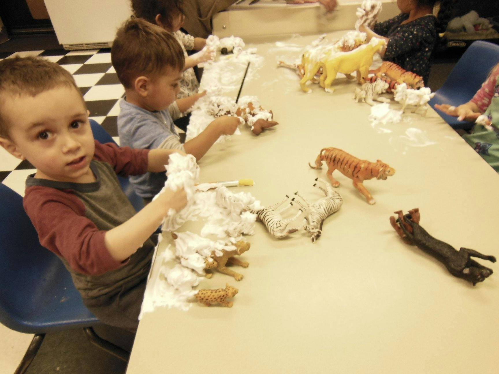 Children playing with shaving cream and animal toys at a table