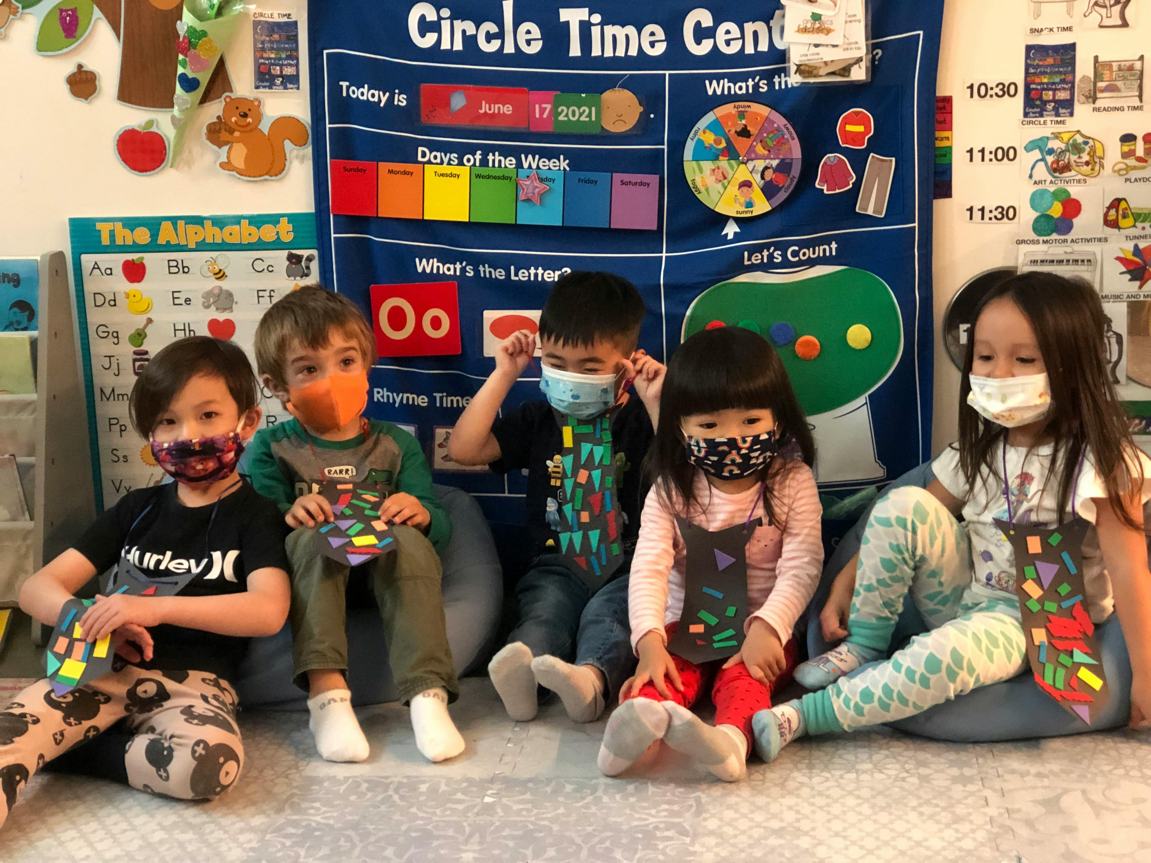 Five children wearing face masks sitting on the floor in a classroom