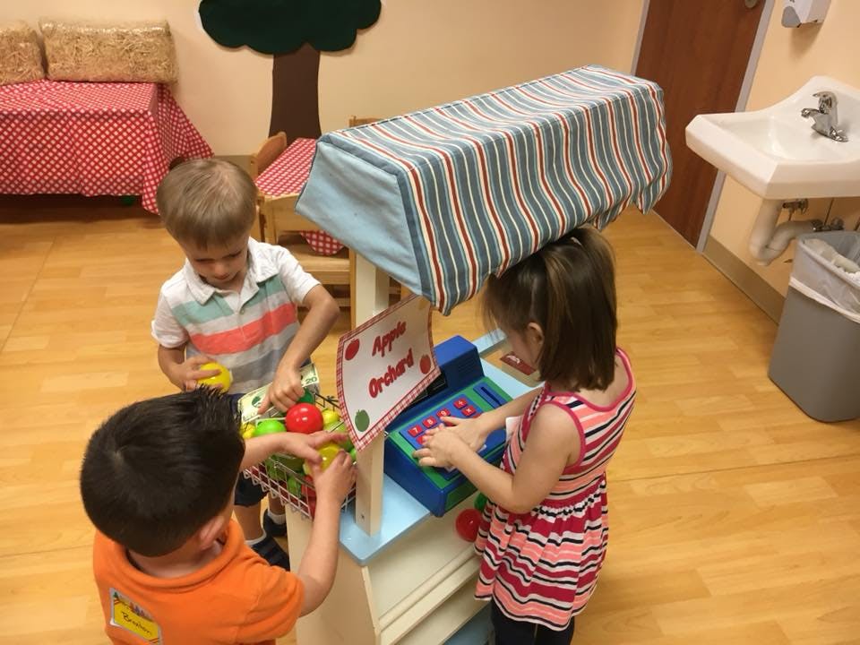 Three children playing with a toy market stand
