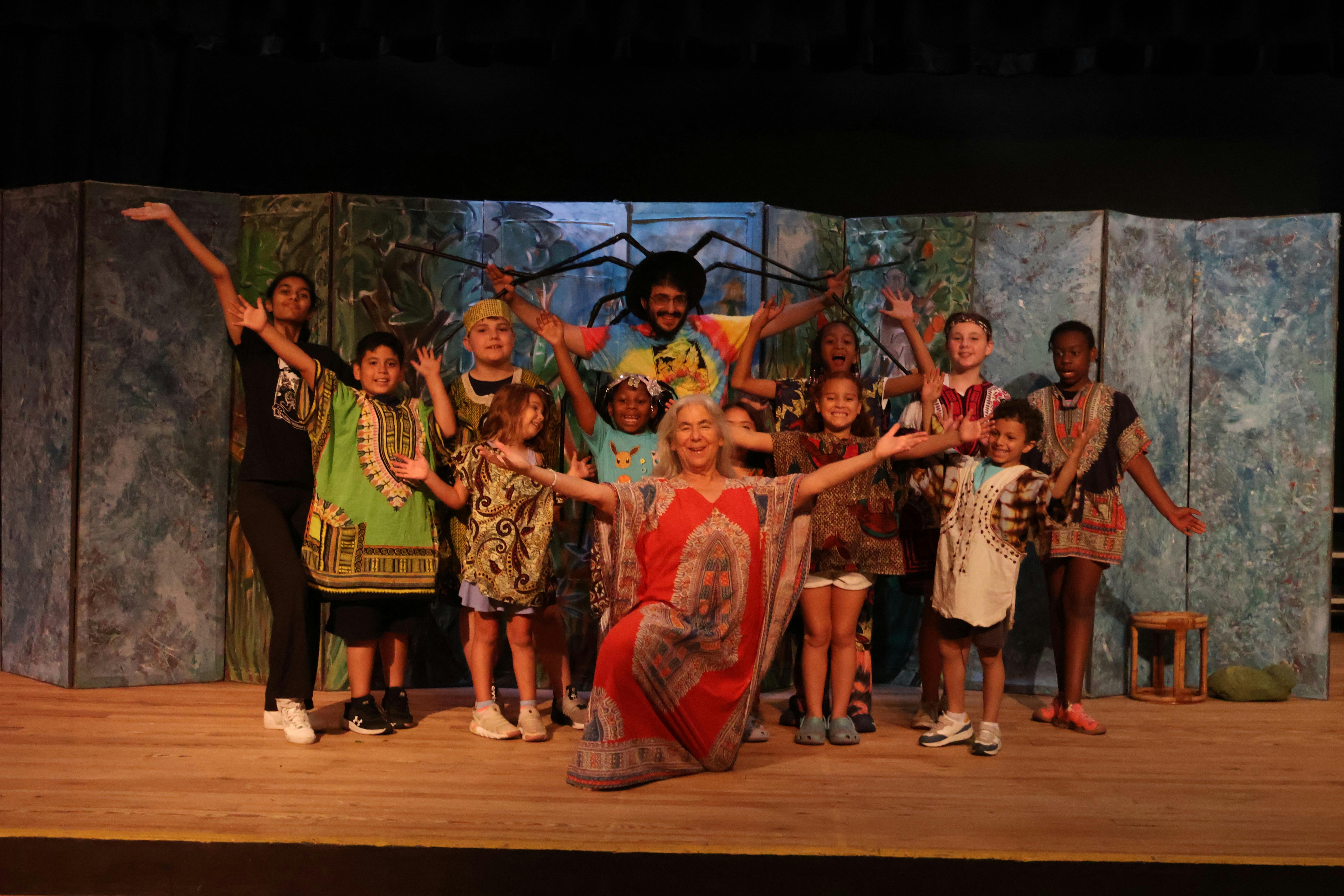 Group of children and adults on a stage with arms raised