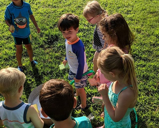 Group of children gathered around an object on the grass