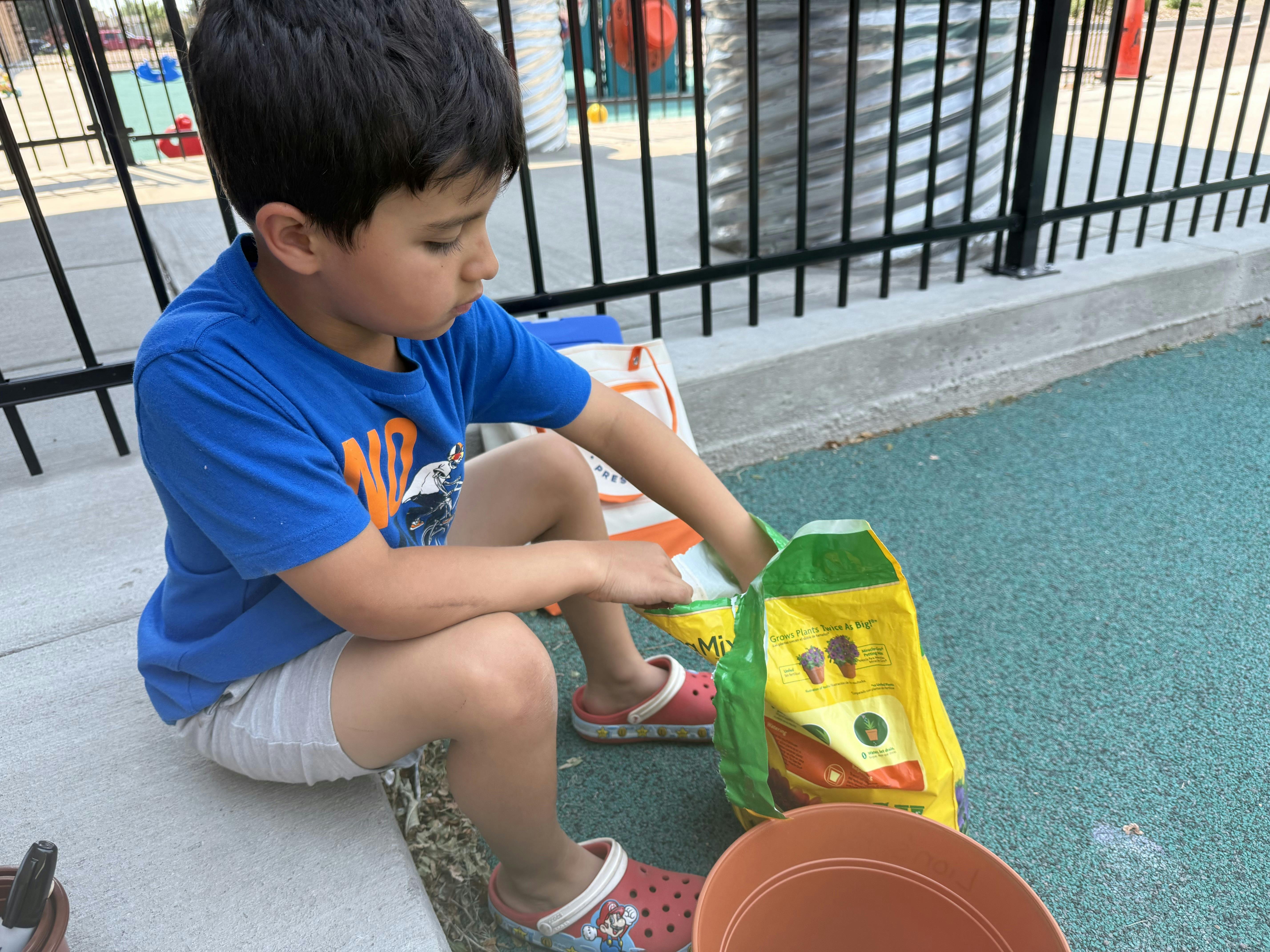 Child sitting on ground filling a flower pot with soil
