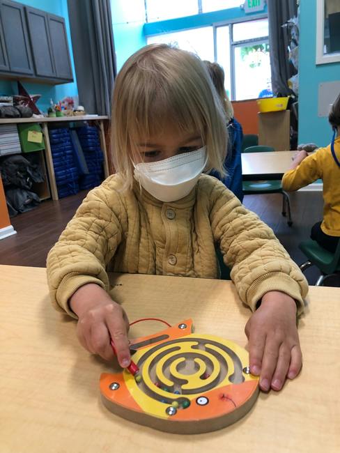 Child in a mask playing with a maze toy on a table