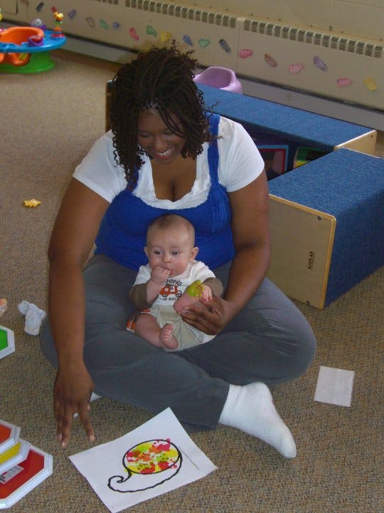 Person sitting on floor holding a child, looking at a drawing