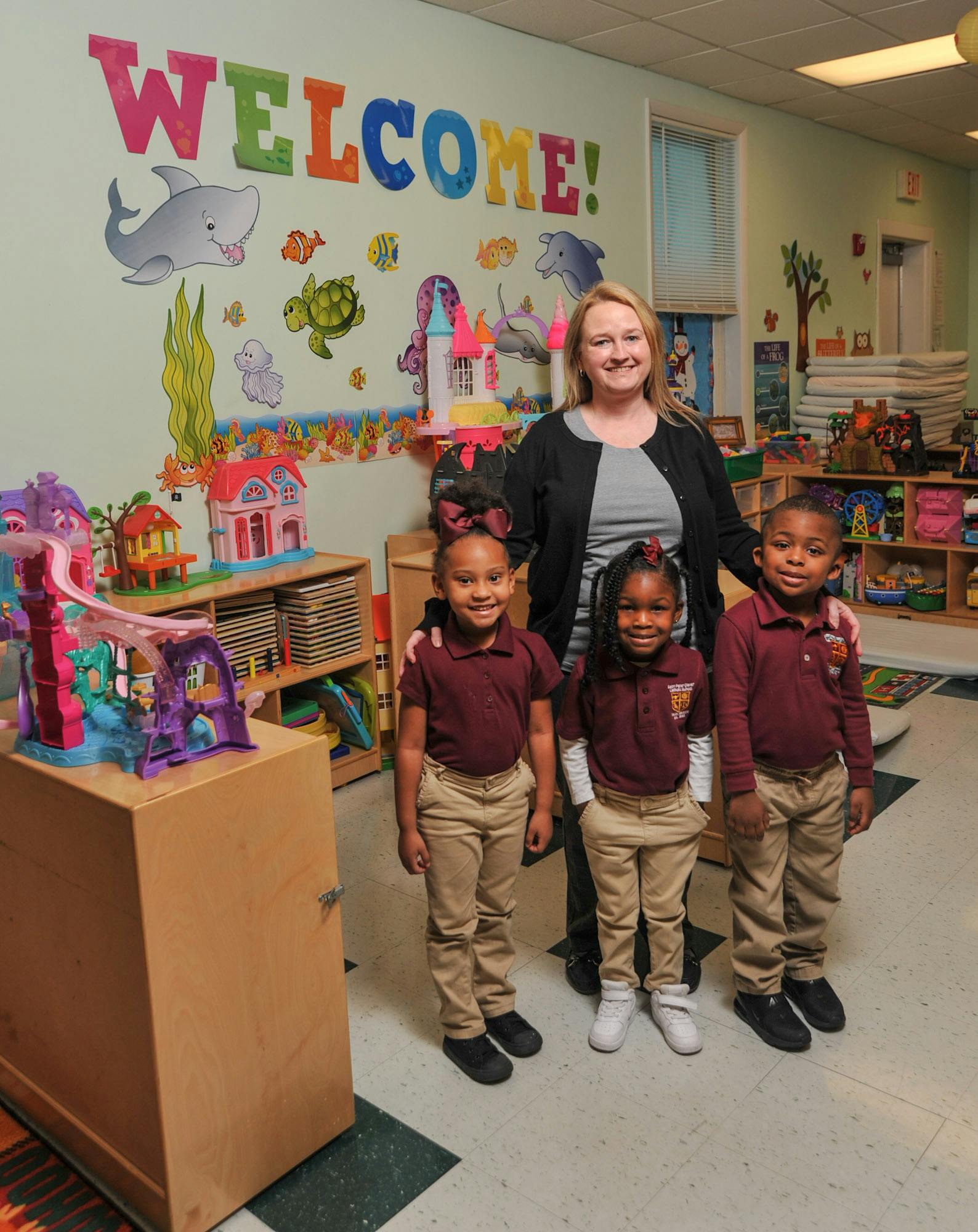 Adult and three children standing in a classroom with "WELCOME" on the wall