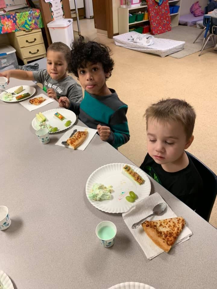 Three children sitting at a table with plates of food