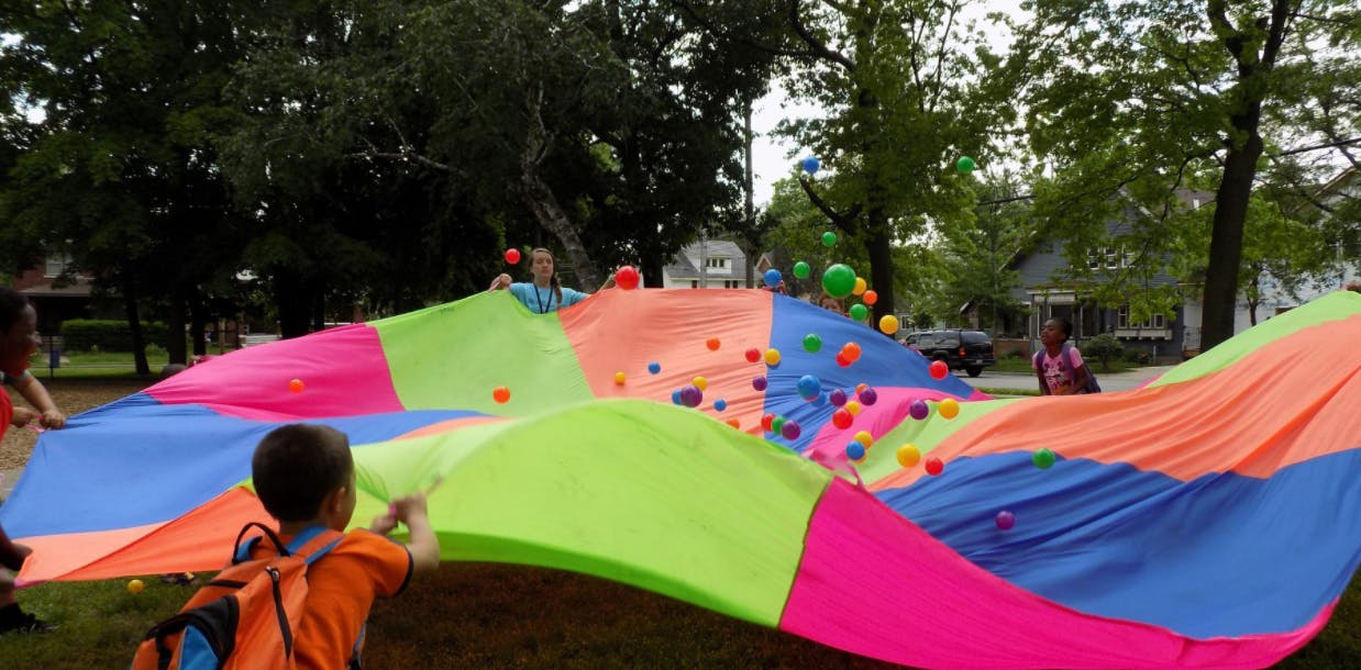 Children playing with a colorful parachute and small balls outdoors