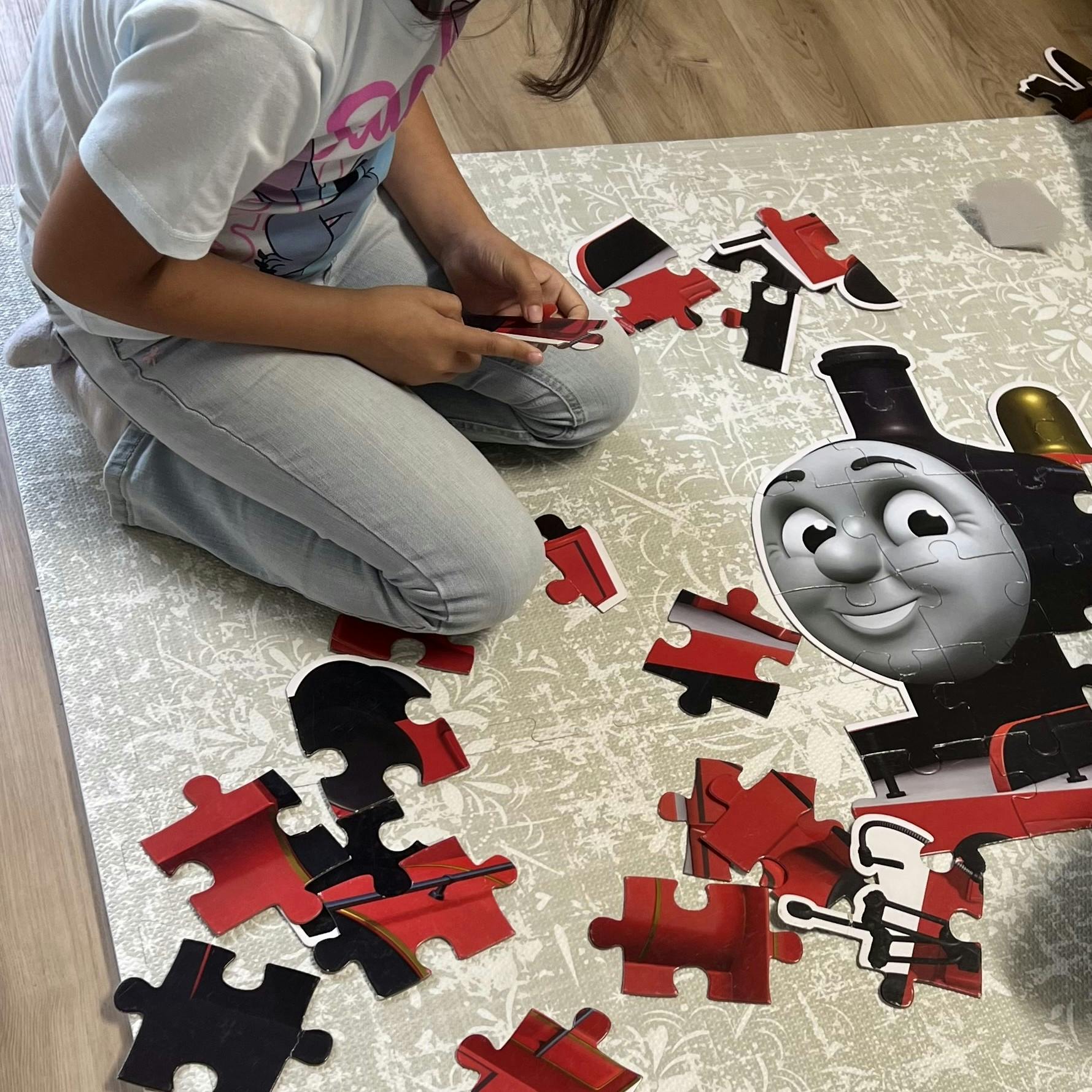 Child on floor assembling a large puzzle of a train