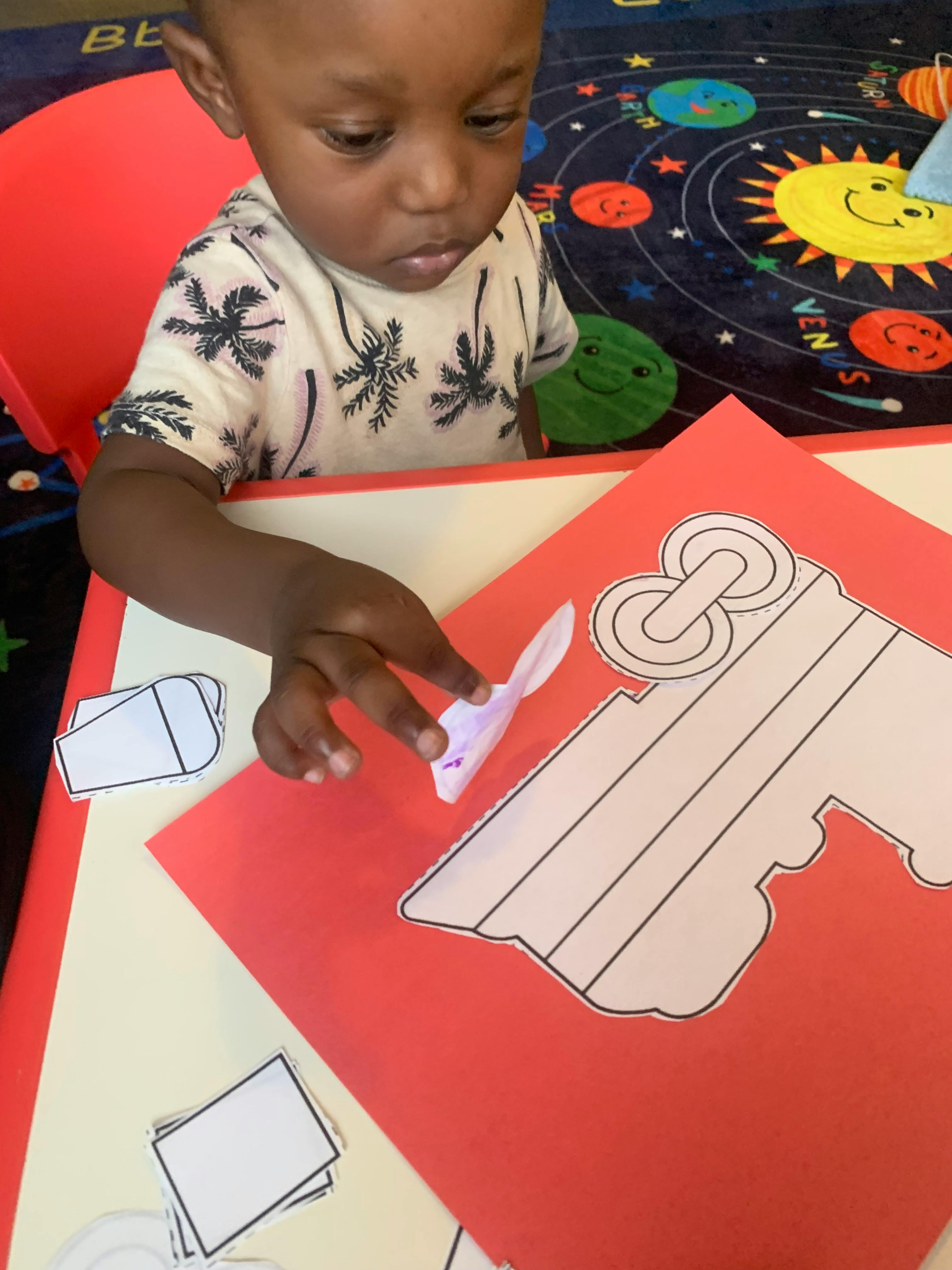 Child playing with paper cutouts on a red and yellow surface