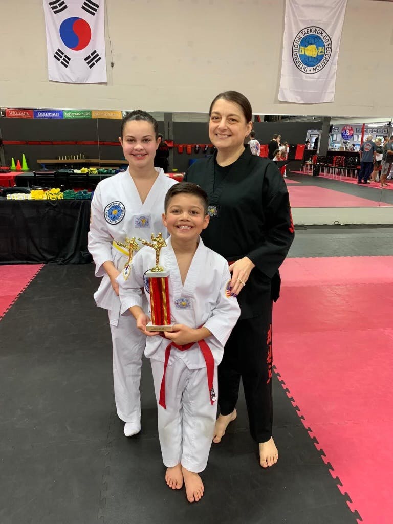 Three people in martial arts uniforms, one child holding a trophy